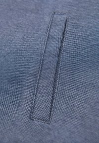 Tejido de denim en un tono azul profundo con una superficie texturizada. Presenta un parche rectangular con costuras visibles.