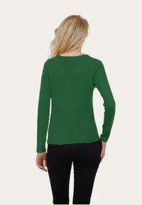Pull vert à manches longues avec un col rond et une silhouette ajustée, fabriqué en tissu tricoté lisse. Porté avec un pantalon noir.