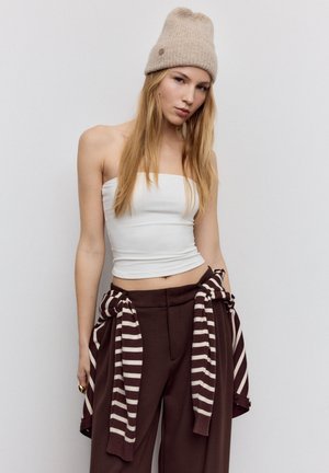 Vit axelbandslös crop top, bruna högmidjade byxor med fickor och en beige stickad mössa. Randig brun och vit tröja knuten i midjan.