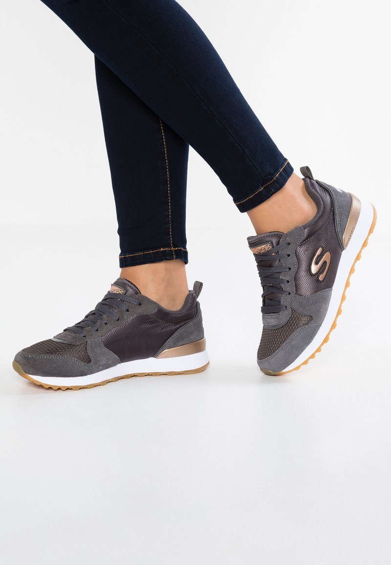 Scarpe sportive di un grigio scuro con pannelli in suede e mesh, dotate di una suola intermedia bianca e una suola esterna in gomma naturale. Design con lacci e accento del logo.