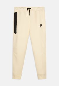 Ljusgråa sweatpants i mjukt material med justerbar svart dragsko, sidoficka med dragkedja och svart Nike-logga på vänster sida. Slät tygtextur.
