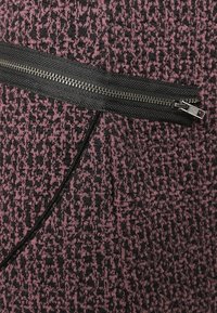 Tessuto texturizzato nero e rosa scuro con un motivo diagonale. Presenta una tasca con zip in un accentato nero solido.