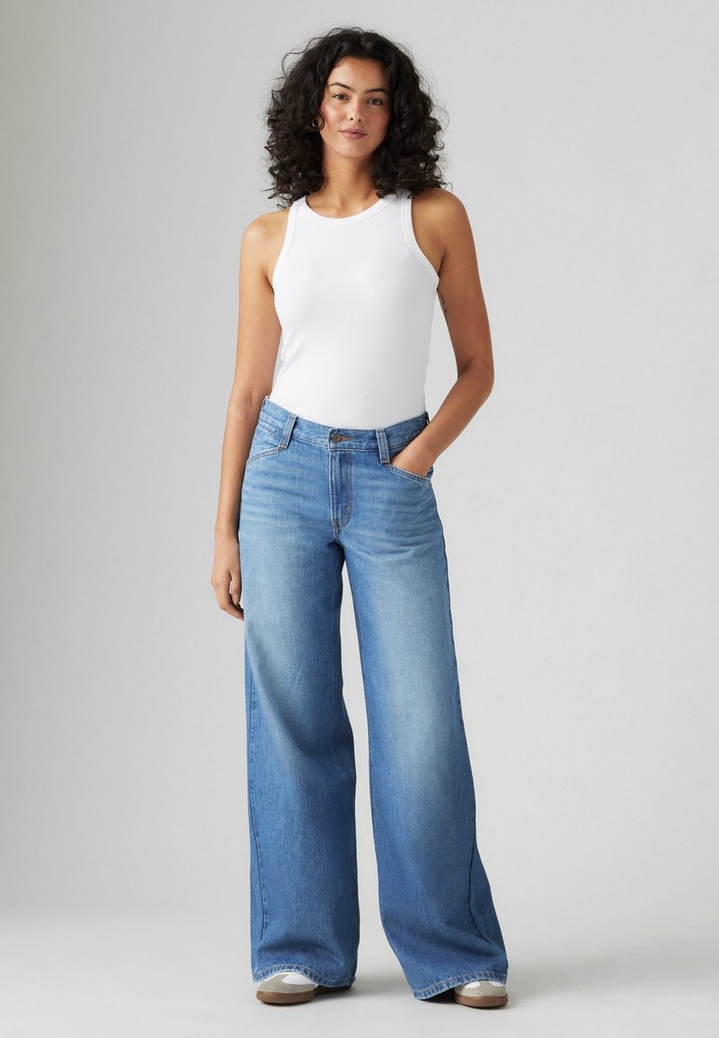 Jeans azzurri a gamba larga con vita alta, abbinati a un top bianco aderente. Tessuto in denim liscio con dettagli minimi.