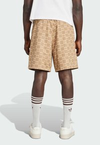 Tan checkered shorts featuring a leaf pattern, elastic waistband, and side pockets, paired with white socks and sneakers.