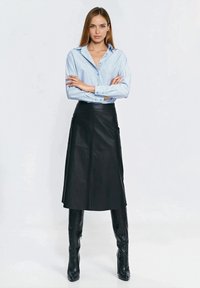 Jasnoniebieska koszula w paski na guziki z długimi rękawami, zestawiona z czarną skórzaną spódnicą do kolan i czarnymi wysokimi kozakami na obcasie.