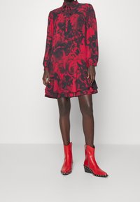 Rode bloemenjurk met lange mouwen en een gerimpelde zoom, gecombineerd met glanzende rode enkellaarzen met zilveren studs en een spitse neus.