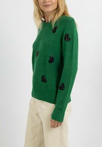 Pull vert en tissu doux, orné de cœurs en sequins noirs disposés uniformément sur le devant, manches longues et poignets côtelés.