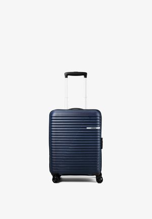 Valigia rigida blu scuro con scanalature orizzontali, quattro ruote e manico telescopico nero esteso, in piedi su sfondo bianco.