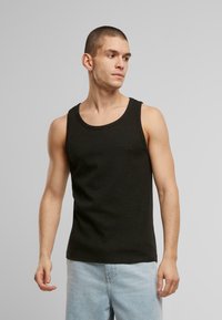 Black tank top made of cotton, featuring a round neck, sleeveless design, and a fitted shape. Paired with light blue jeans.