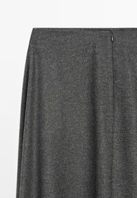 Tissu gris foncé avec un tissage finement texturé et une petite boucle ou bouton en métal sur le côté près du bord supérieur.
