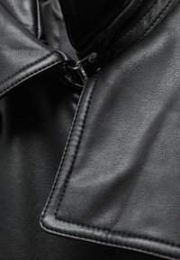 Černá kožená bunda s detailním záběrem na límec a zip. Vyznačuje se hladkým povrchem, výrazným prošíváním a lesklými kovovými doplňky.
