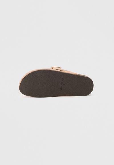 Rjavi nubuk sandal s zaobljenim nosom, ravnim teksturiranim podplatom in kovinskim detajlom na zaponki. Spodnji del je opremljen z trdnimi črnimi zarezami.