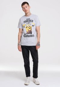 Gray graphic t-shirt featuring a Minion with bananas; black jeans; white high-top sneakers. Simple, casual design with bold print.