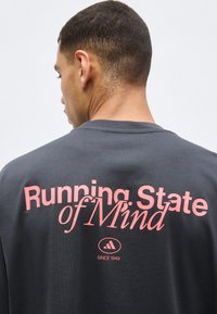 Homme aux cheveux courts de dos, portant un t-shirt gris foncé avec un texte rose « Running State of Mind » et un petit logo en dessous.