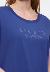 Niebieska koszulka z krótkim rękawem i okrągłym dekoltem, z ozdobnym motywem faz księżyca oraz napisem "by the light of the Moon".