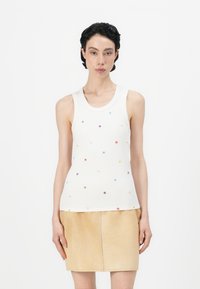 Witte geribbelde tanktop met kleurrijke bloemenborduursels, gecombineerd met een beige leren minirok. Eenvoudig ontwerp en een aansluitende silhoët.
