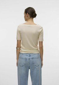 Beige tætsiddende top med korte ærmer, glat tekstur, rund hals, parret med lyseblå brede jeans med baglommer og klassisk denim finish.