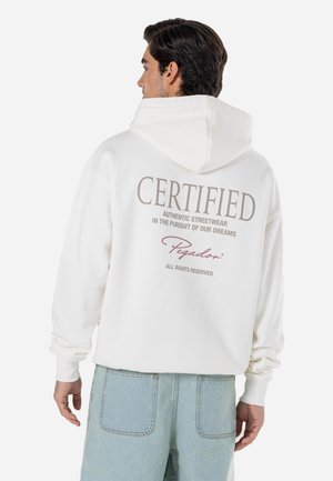 White hoodie with a large "CERTIFIED" text on the back. Features a drawstring hood, ribbed cuffs, and relaxed fit. Paired with light blue pants.