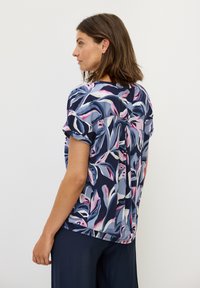 Top a maniche corte floreale in blu navy, con un motivo vivace di foglie rosa e blu. Tessuto leggero con una vestibilità rilassata e orlo arrotondato.