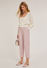Cardigan en tricot crème, pantalon ajusté rose clair et ballerines rose pâle avec des accents dorés. Petit sac à main avec un motif rose et crème.