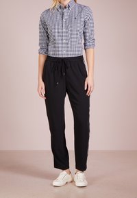 Pantaloni jogger neri con vita regolabile. Abbinati a una camicia button-up a quadri blu e bianchi. Sneakers bianche completano l'outfit.