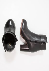 Botas de tobillo de cuero negro con textura suave, punta redonda, cremallera lateral y un tacón ancho de madera. Diseño minimalista sin acentos adicionales.