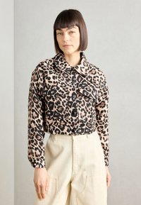 Kuttet leopardmønstret jakke i beige og svart, med skjortekrage, knappelukking og to brystlommer. Glatt tekstur.