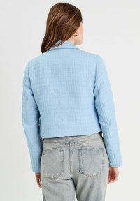 Veste crop bleu clair avec une finition texturée, dotée d'un col et de manches longues, associée à un jean en denim taille haute.
