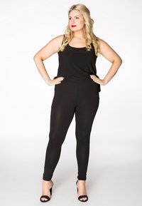 Zwarte mouwloze top gecombineerd met zwarte leggings, beide met een gladde, aansluitende textuur. Model draagt zwarte hakken. Eenvoudig ontwerp.