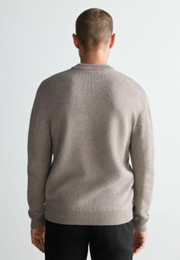 Szary sweter dzianinowy z okrągłym dekoltem i ściągaczami, wykonany z teksturowanej, miękkiej tkaniny. Prosty design, noszony z czarnymi spodniami.
