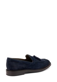 Mocassino in suede blu navy con punta rotonda e pon-pon decorativi. Presenta dettagli cuciti e una suola piatta marrone.