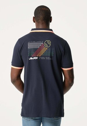 Polo shirt bleu marine avec un graphique de tennis rétro coloré au dos, des poignets contrastants rose-orange et un col classique.