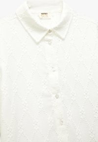 Camisa blanca para niño con un patrón de diamantes, diseño de botones y cuello, hecha de tela texturizada.