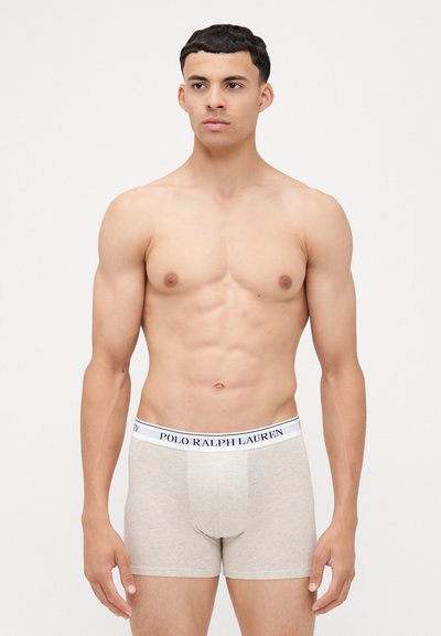 Bež bokserice iz mehke bombažne tkanine, ki imajo širok bel pas z napisom "POLO RALPH LAUREN" v mornarsko modri barvi.