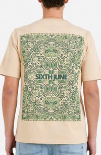 Camiseta de algodón beige con un gran patrón de paisley verde en la parte posterior, con "SIXTH JUNE" impreso en verde oscuro en el centro.