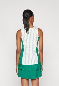 Grön och vit sportklänning med vertikala ränder, ärmlös design, volangnedkant och texturerad tyg. Visas bakifrån.