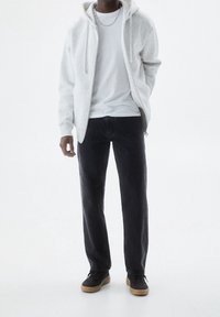Sudadera con cremallera de color gris claro sobre una camiseta blanca, combinada con jeans oscuros y zapatillas negras con suelas de goma, con un diseño minimalista.