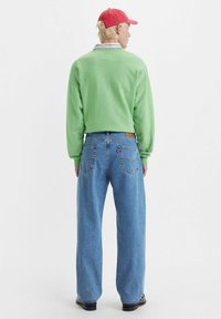 Suéter verde de punto con cuello redondo, combinado con unos vaqueros de denim de corte holgado en un tono azul claro y una gorra de béisbol roja. Diseño simple y ajuste casual.