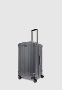 Grauer Hartschalenkoffer mit vertikalen Rillen, einem ausziehbaren schwarzen Griff und vier schwarzen Rollen. Verfügt über seitliche und obere Griffe.