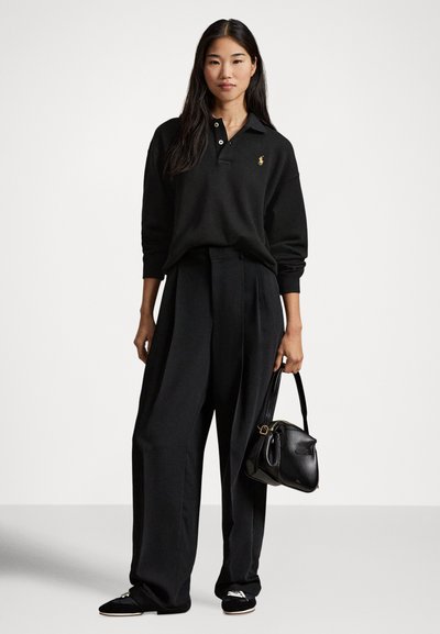 Črna polo majica z ovratnikom, veliki kroj; črne hlače z naborki; mala črna torbica; črni loaferji z dekorativnim poudarkom.