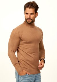Brauner Rollkragenpullover aus einem glatten Strickstoff, taillierte Passform, mit langen Ärmeln und gerippten Bündchen, kombiniert mit hellblauen Jeans.