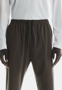 Brown athletic pants with an elastic waistband, black drawstring, and smooth texture, paired with a white long-sleeve shirt.