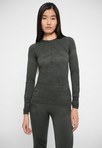 Top da attivita a maniche lunghe di colore verde scuro, con motivi testurizzati e design aderente. Realizzato in un tessuto elastico e traspirante.