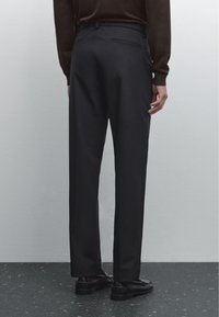 Pantaloni formali neri con una vestibilità su misura, caratterizzati da una gamba dritta, una tasca posteriore discreta e un tessuto dalla finitura liscia. Abbinati a scarpe nere.