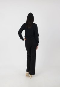 Jersey negro de punto con detalles acanalados, combinado con jeans negros de pierna ancha de cintura alta y zapatos de tacón bloque en color crema. Look simple y monocromático.