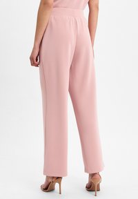 Helle rosa weite Hosen mit elastischem Bund, ausgestattet mit einer glatten Textur und seitlichen Nähten. Kombiniert mit nudefarbenen High Heels.