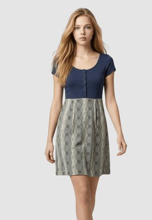 Joven mujer con cabello rubio largo que lleva un vestido azul marino de manga corta con una falda gris con estampado, de pie contra un fondo claro.