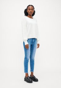 Pulover alb cu mâneci texturate, blugi bleu deschis, ajustați, și pantofi platform negri, cu tălpi groase, decorați cu ținte argintii, purtați de o persoană în picioare.