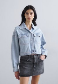 Kratka svetlo modra jeans jakna z dvema sprednjima žepoma in gumbnim zapiranjem, v kombinaciji z črno jeans krilom z visokim pasom.