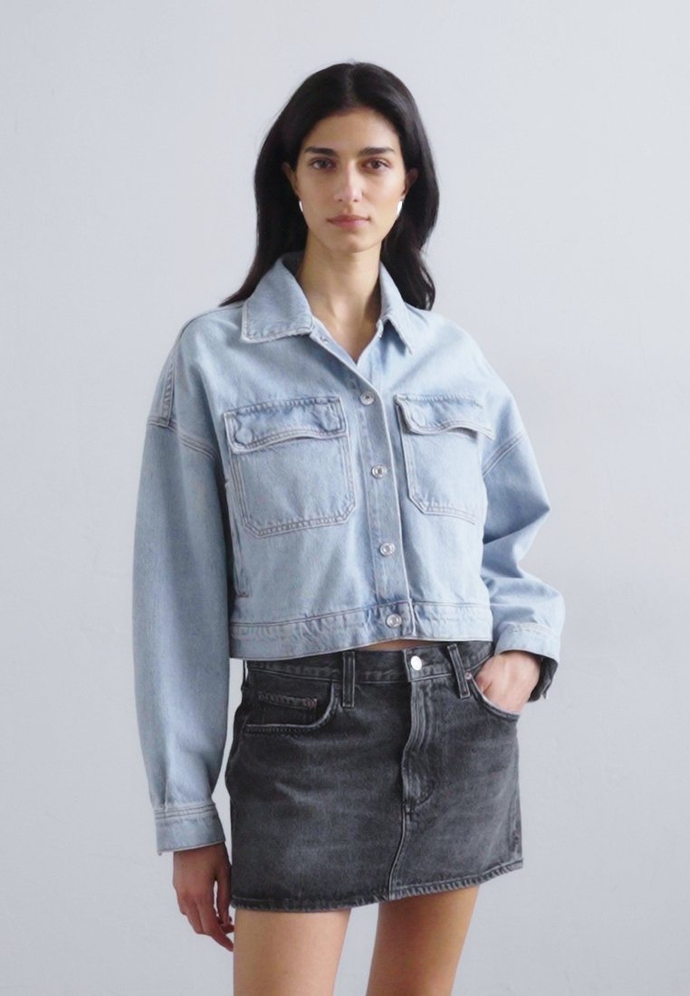 Veste en denim bleu clair coupée avec deux poches avant et fermeture à boutons, associée à une jupe en denim noire taille haute.